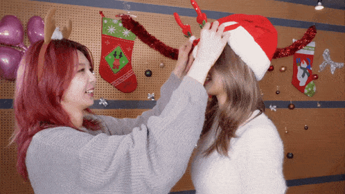 a christmas stocking with a reindeer on it hangs on a wall behind two women wearing santa hats