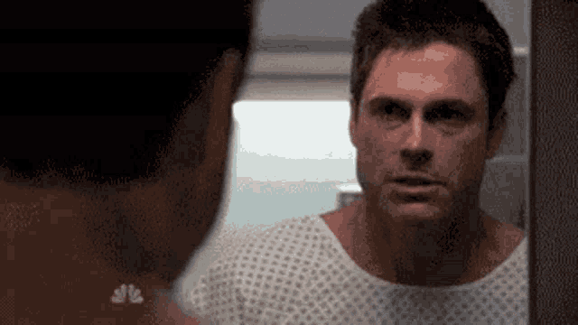 a man in a hospital gown looks at himself in a mirror .