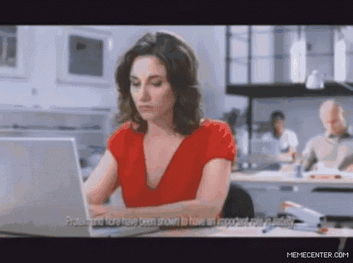 a woman in a red shirt sits at a desk with a laptop