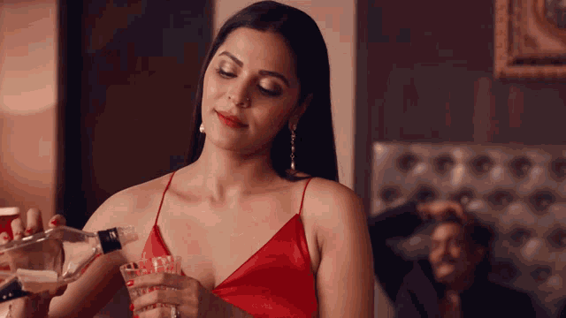 a woman in a red dress is holding a glass and a bottle of vodka
