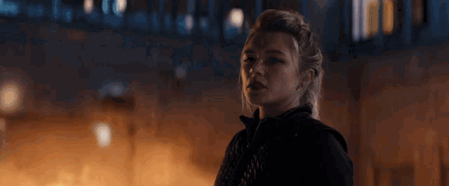 a woman in a black jacket is standing in front of a fire at night .