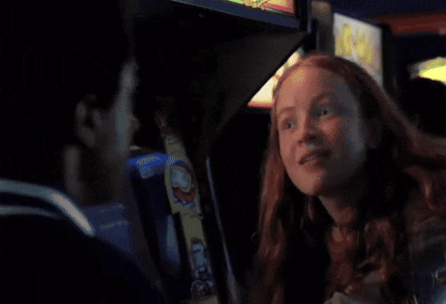 a woman with red hair is sitting in front of an arcade machine