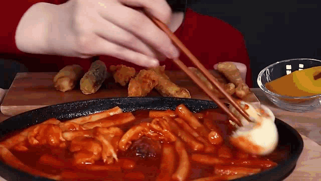 a person is eating a plate of food with chopsticks and a bowl of sauce .