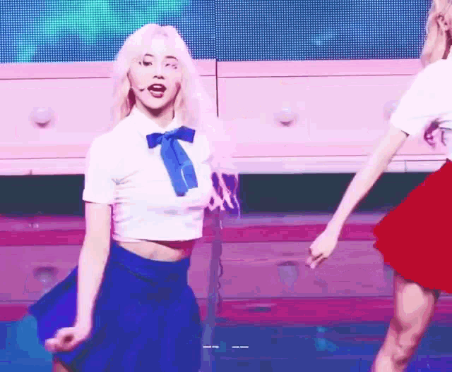 a girl in a white shirt and blue skirt is dancing on a stage .
