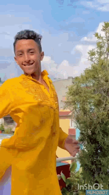 a young man wearing a yellow shirt is standing in front of a tree .