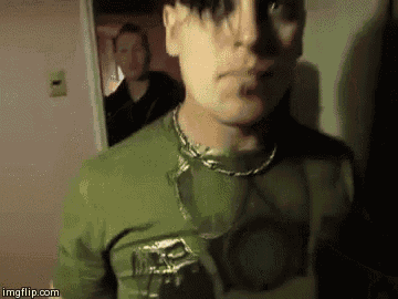 a man wearing a green shirt and a chain around his neck is standing in front of a door .