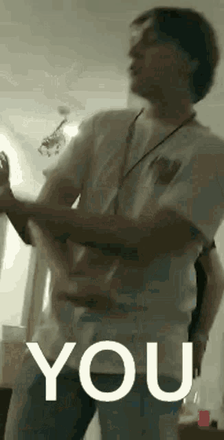 a man in a white shirt is dancing in a room with the word you written on the bottom .