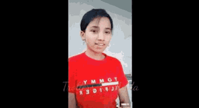 a young girl wearing a red t-shirt is making a funny face .
