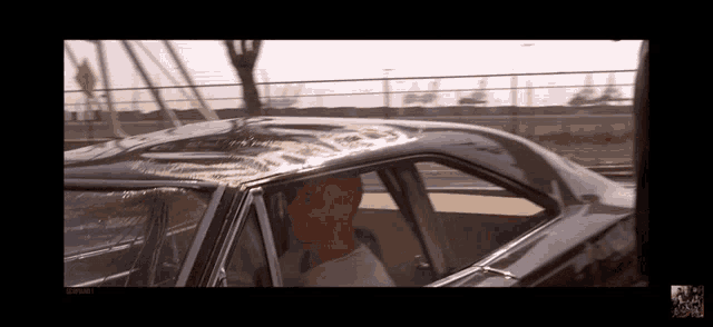 a man is sitting in a car with a reflection of a bridge