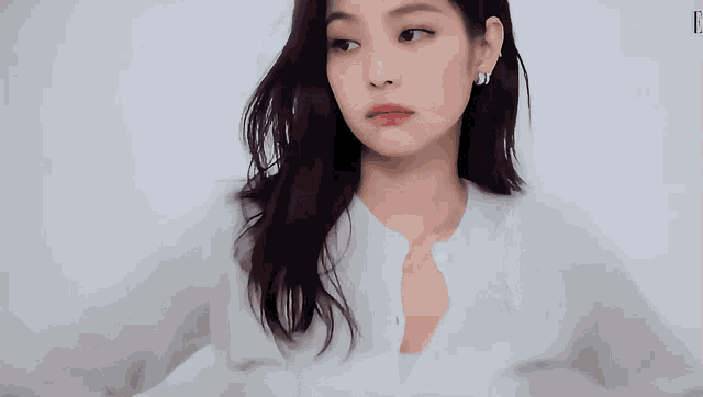 a woman wearing a white shirt and earrings looks to the side