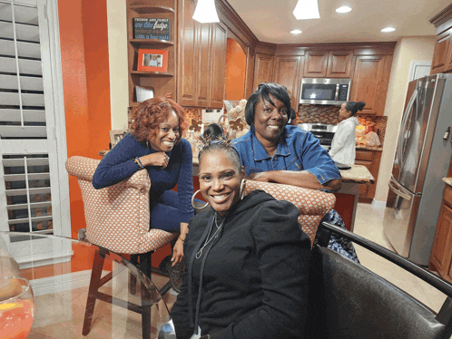 three women are sitting in a kitchen with a sign on the wall that says " tomorrow and today are the days "