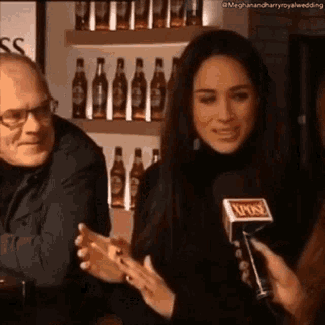 a woman is talking into a microphone in front of a man and bottles of beer .