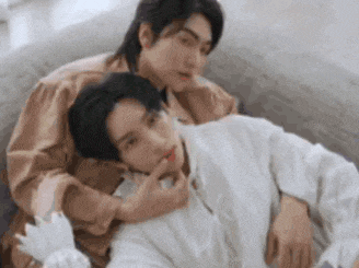 two young men are laying on a couch and one is touching the other 's neck .