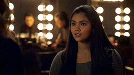 a woman with long dark hair is standing in front of a mirror with lights on it