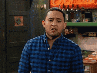 a man in a blue plaid shirt is making a funny face in a kitchen .