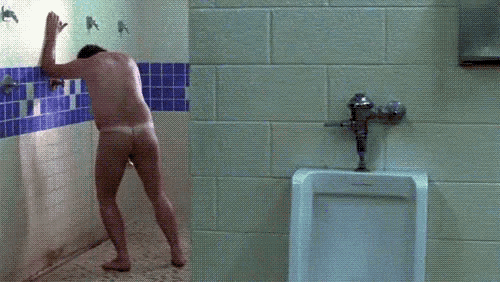 a naked man stands in a bathroom next to a urinal with the letter a on the wall