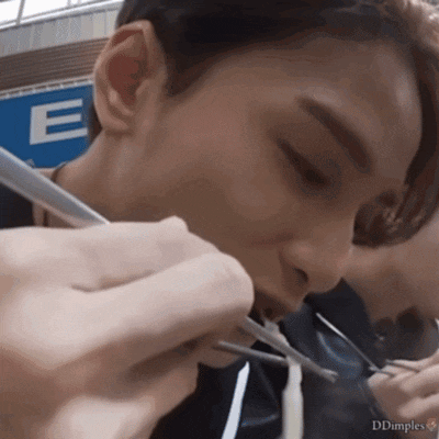 a close up of a person eating with chopsticks in front of a blue sign that says e