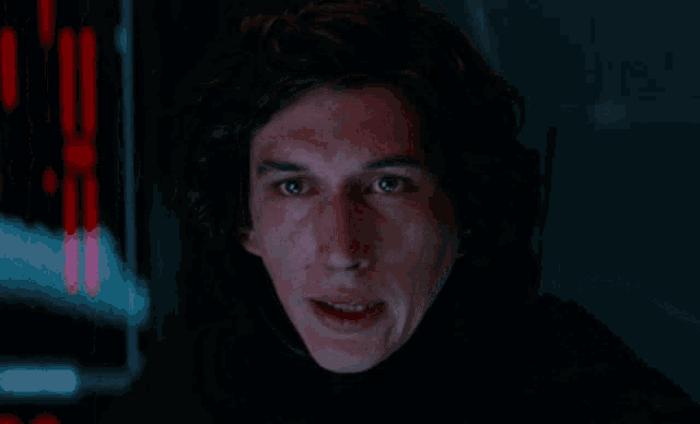 a close up of a man 's face in a dark room with red lights behind him