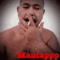 a man without a shirt is covering his mouth with his hands while smoking a cigarette .