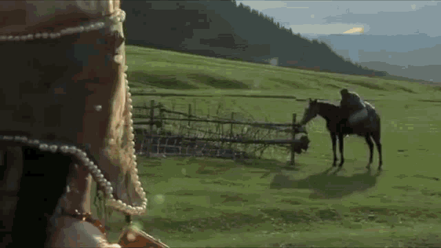 a man riding a horse in a field with a fence in the background
