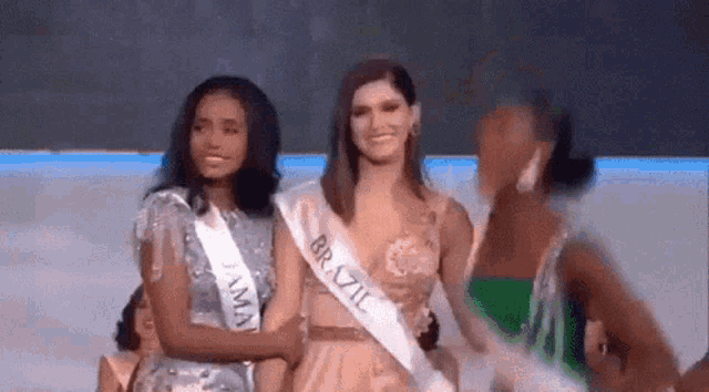 a group of women are standing next to each other and one of them is wearing a sash that says brazil on it .