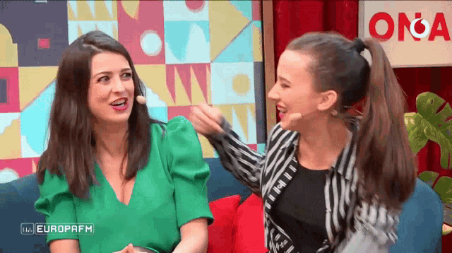 two women are sitting on a couch with a sign that says europafm
