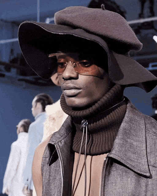 a man wearing a hat and sunglasses is standing in front of a group of people