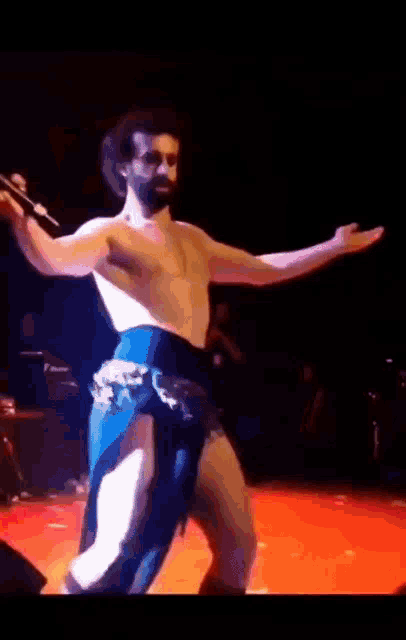 a shirtless man is dancing on a stage with a microphone