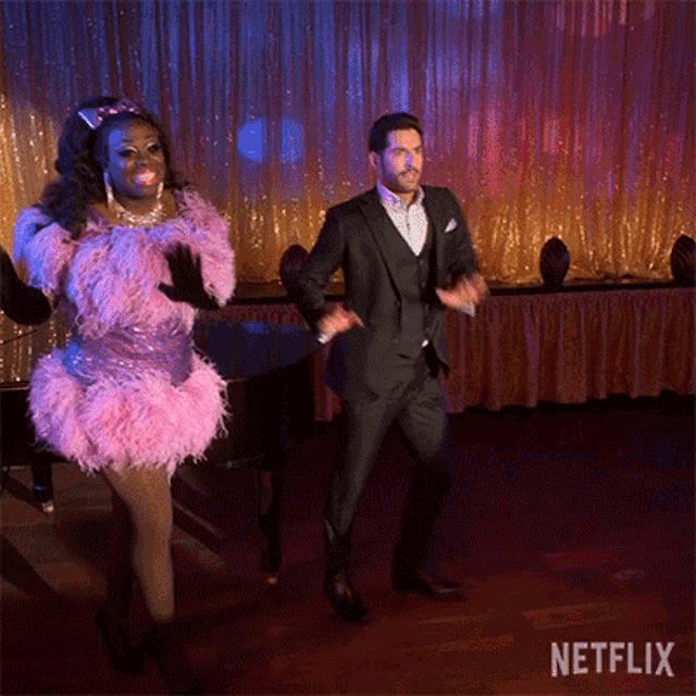a man in a suit is dancing with a woman in a pink dress .