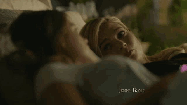 two women are laying on a couch looking at something