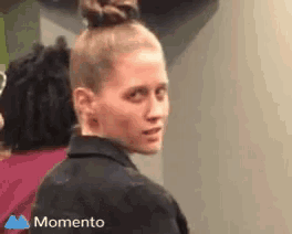 a woman with a bun on her head is looking at the camera with a momento logo in the corner