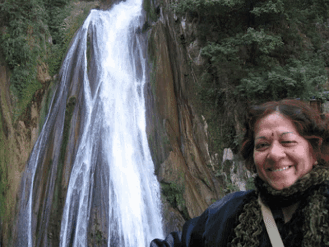 a woman stands in front of a waterfall and smiles