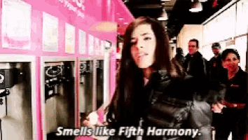 a woman is standing in front of a machine that says smells like fifth harmony