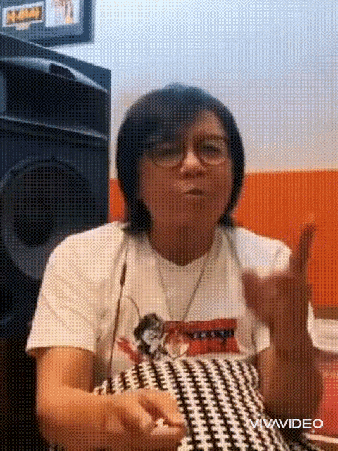 a woman wearing glasses and a white t-shirt is sitting in front of a speaker .
