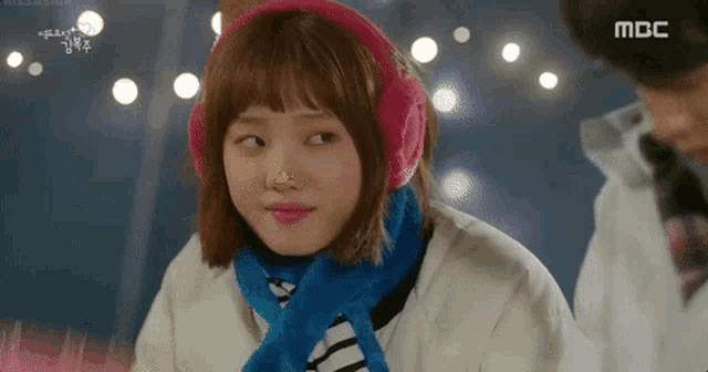 a woman wearing pink ear warmers and a blue scarf is looking at a man .