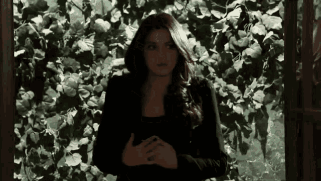 a woman is standing in front of a leafy wall