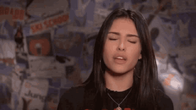 a woman with long hair is making a funny face in front of a wall with posters on it .