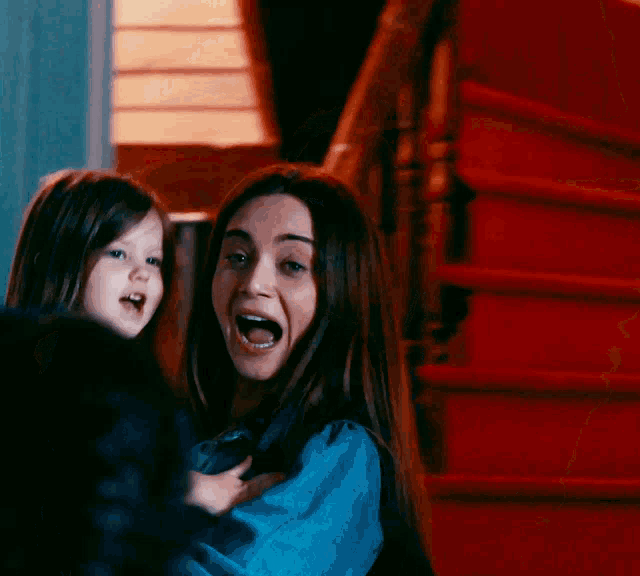 a woman in a blue shirt is holding a little girl