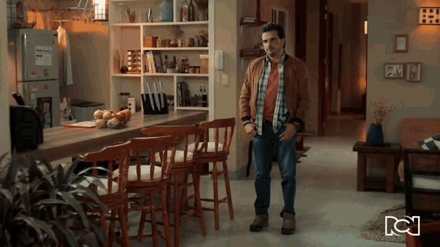 a man in a plaid shirt stands in a living room with a nc logo on the wall
