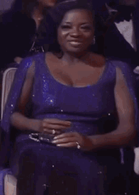 a woman in a purple dress is smiling while sitting in a chair