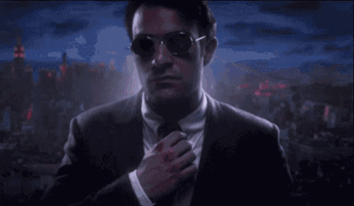 a man in a suit and tie with blood on his shirt is adjusting his tie .