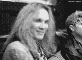 a woman with long hair is smiling in a black and white photo while sitting next to a man .