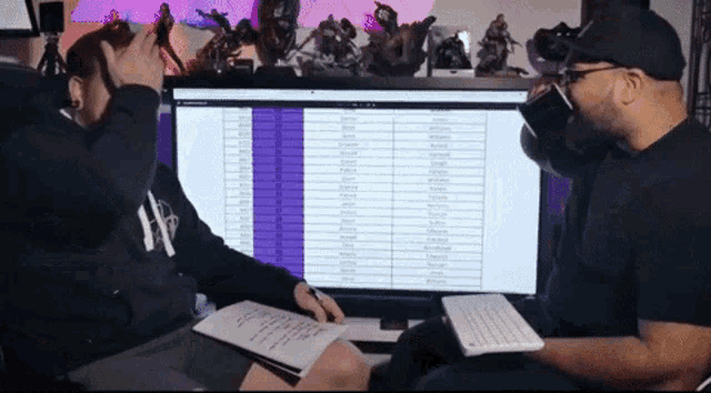 two men are sitting in front of a computer screen with a list of names