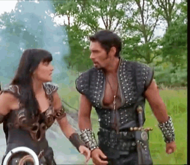 a man and a woman are standing next to each other in a field holding hands and talking .