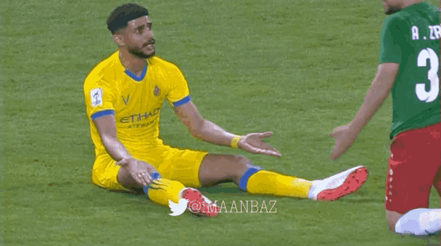 a soccer player in a yellow etihad jersey sits on the ground