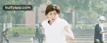 a woman in a white shirt is running in a park with a man in a hat in the background .