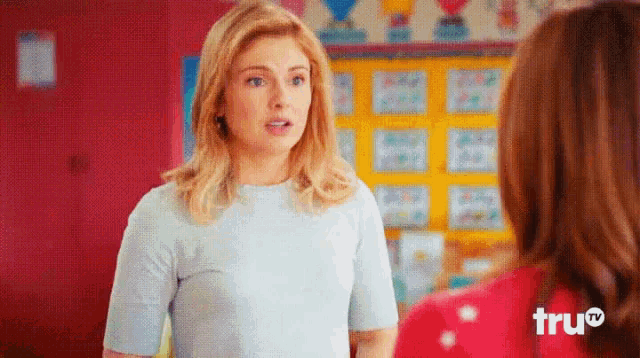 a woman in a blue shirt is standing next to another woman in a red shirt with the word true on the bottom left