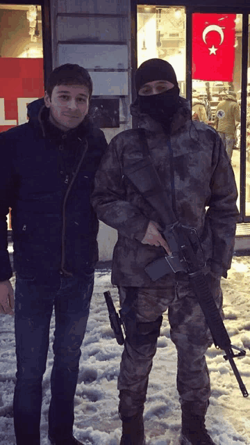 a man in a mask stands next to a man in a military uniform with a gun