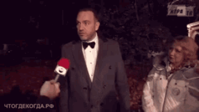 a man in a suit and bow tie is talking into a microphone