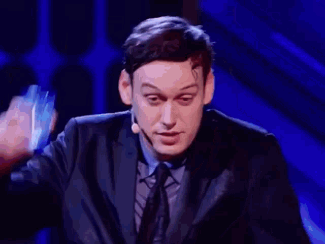 a man in a suit and tie is standing in front of a microphone on a stage holding a glass .